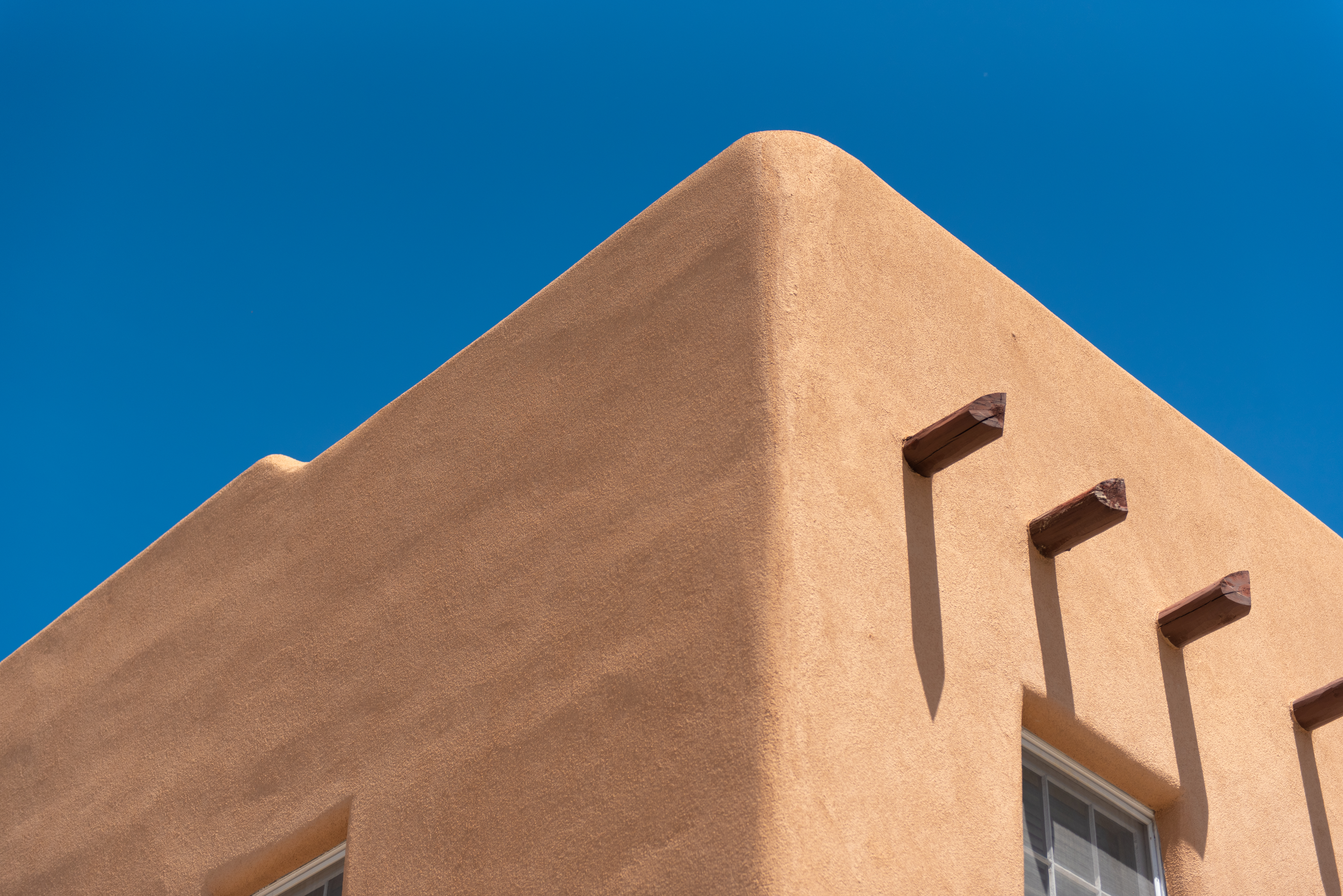 Adobe corner with projecting vigas against a deep blue sky